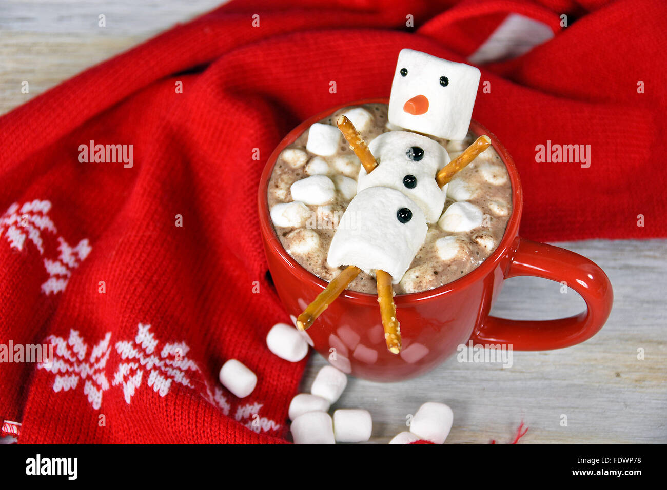 Hot chocolate drink with marshmallow snowman in red mug with red winter scarf. Stock Photo