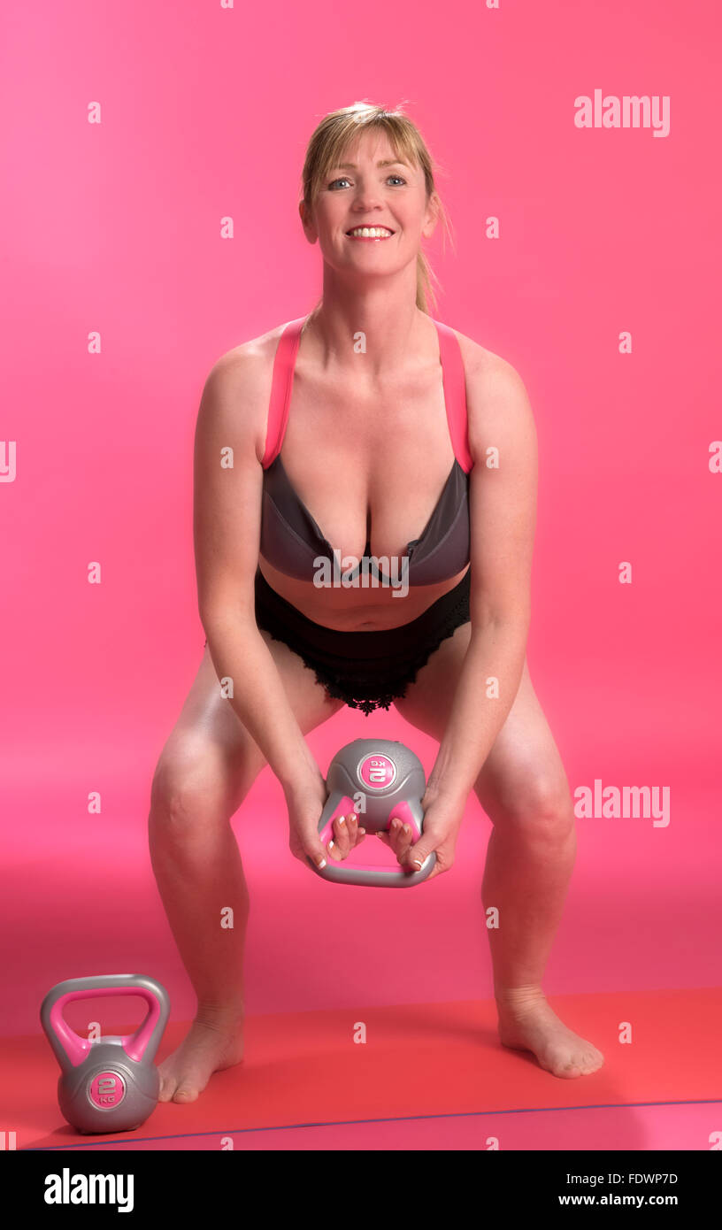 Woman with bent knees using a kettle bell to exercise Stock Photo