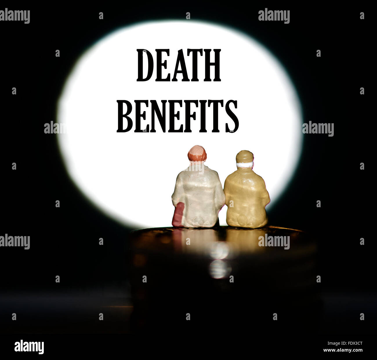 Miniature figurine pensioners sitting on coins in front of a spotlight showing the word death benefits concept Stock Photo