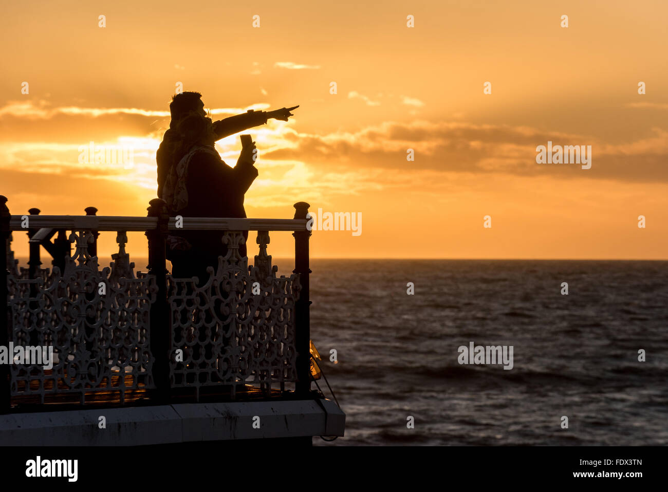 Two people watching the sunset off Brighton's Palace Pier. Stock Photo