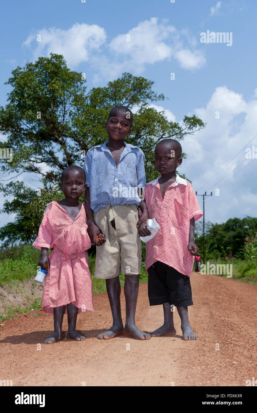 Young children walking barefoot down a dirt road on their way home from school, Uganda. Stock Photo