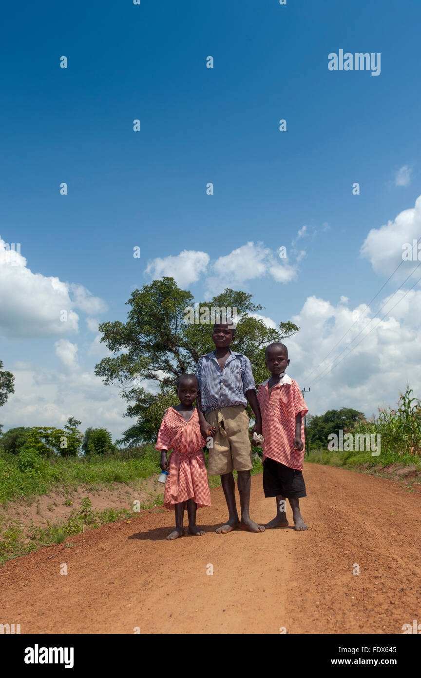 Young children walking barefoot down a dirt road on their way home from school, Uganda. Stock Photo