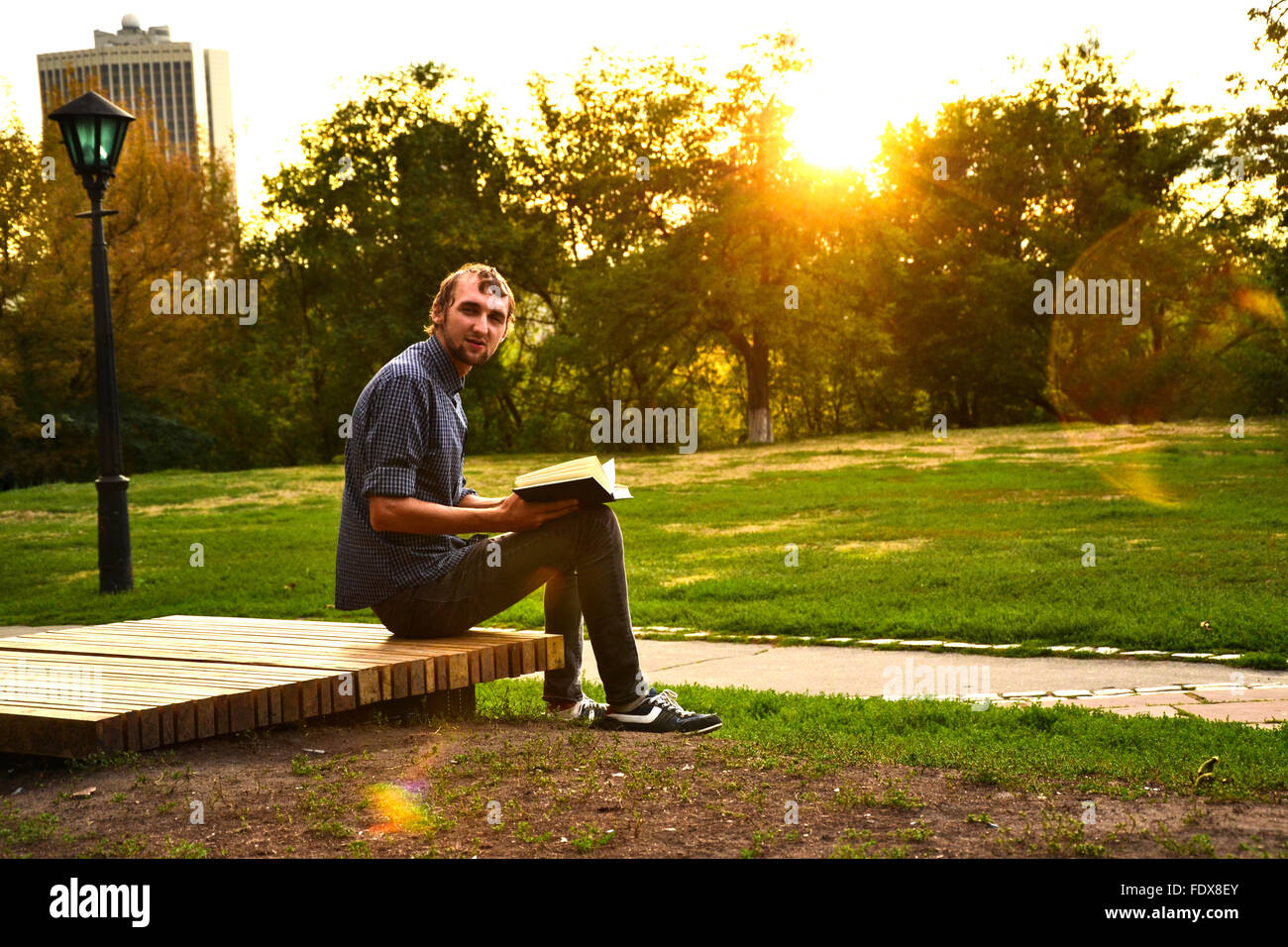 Guy sitting on a bench in the park reading book Stock Photo