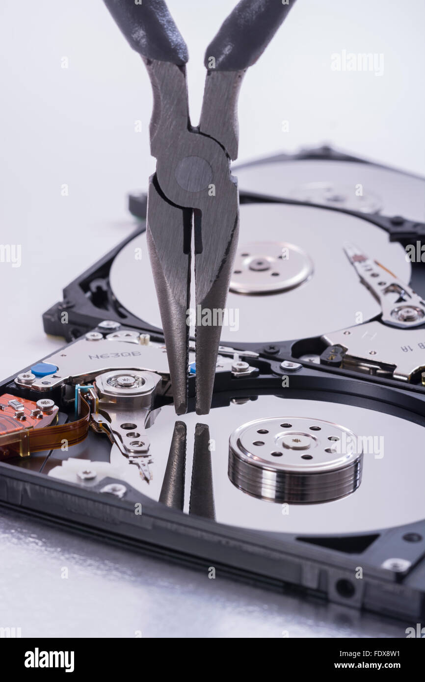 Pair of DIY pincers poised over platter of a stripped hard disk drive - visual metaphor for concept of software tools, IT tools. Stock Photo