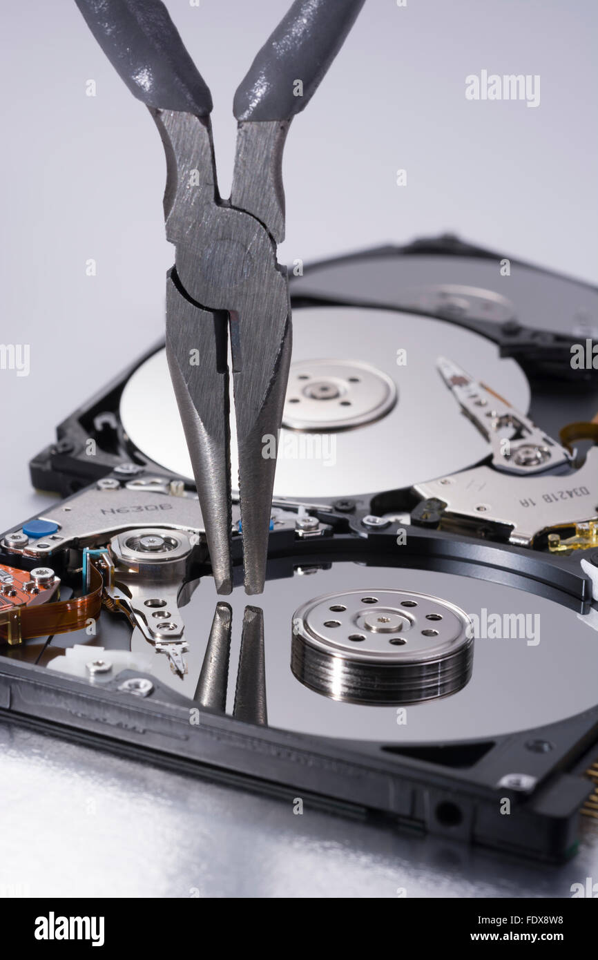 Pair of DIY pincers poised over platter of a stripped hard disk drive - visual metaphor for concept of software tools, IT tools. Stock Photo