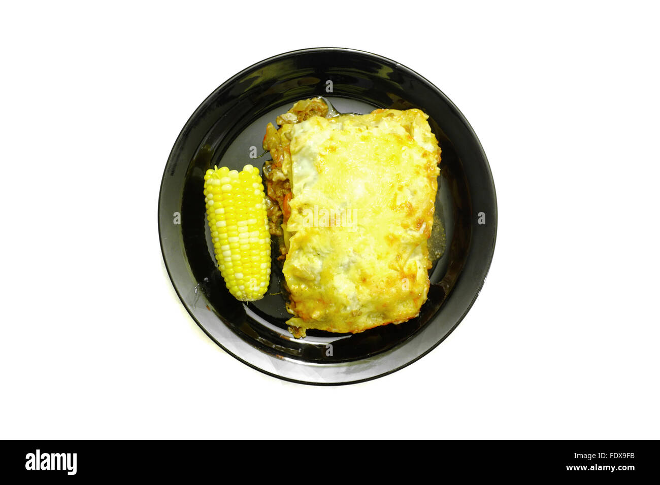Lasagna and sweetcorn on a black plate photographed against a white background Stock Photo
