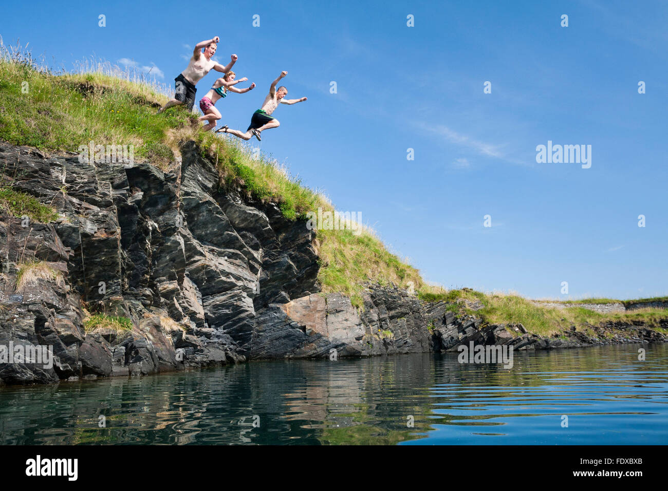 Three people jumping into old quarry pool, Belnahua, Highland, Scotland, United Kingdom Stock Photo