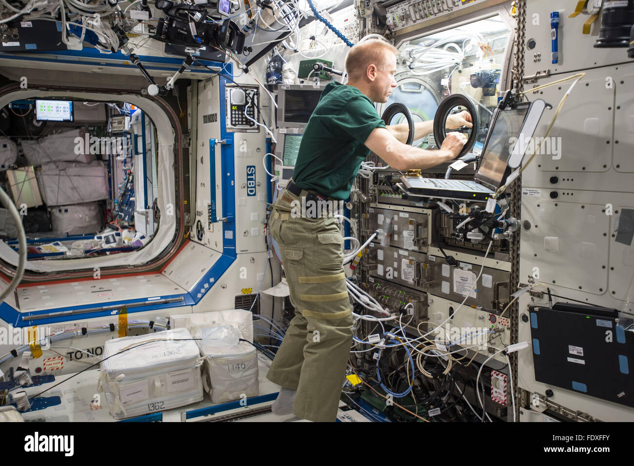 NASA astronaut Tim Kopra sets up hardware for the Burning and Suppression of Solids Ð Milliken, or BASS-M, experiment aboard the International Space Station January 27, 2016 in Earth Orbit. The BASS-M investigation tests flame-retardant cotton fabrics to determine how well they resist burning in microgravity. Stock Photo
