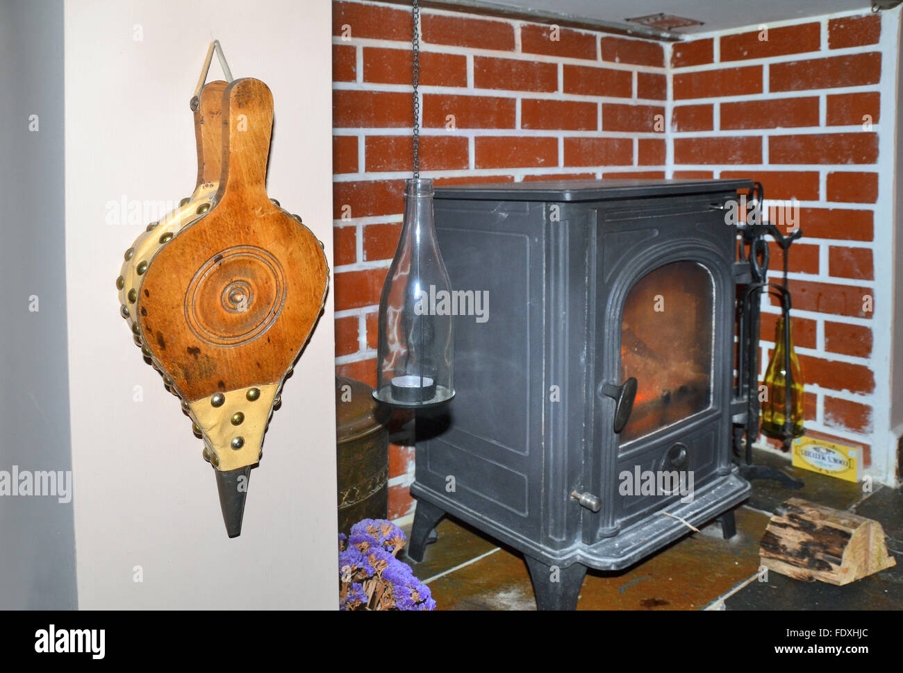 wooden fire bellows hanging close to an indoor wood burning stove situated in converted fireplace. Stock Photo