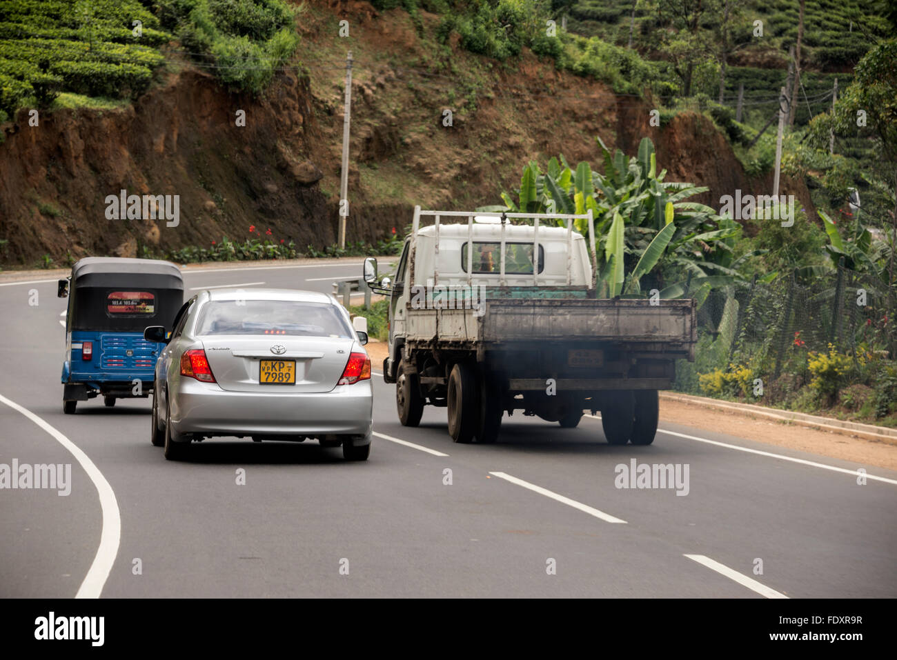 A pickup truck belching out the polluted exhaust of diesel fumes as it overtakes other vehicles whilst approaching  a sharp bend Stock Photo