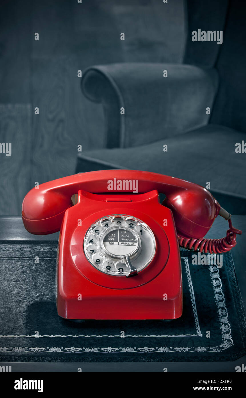 HOTLINE 70s red dial telephone style fashion classic sales HOT LINE retro office GPO BT red phone handset antique desk mono background & vintage chair Stock Photo