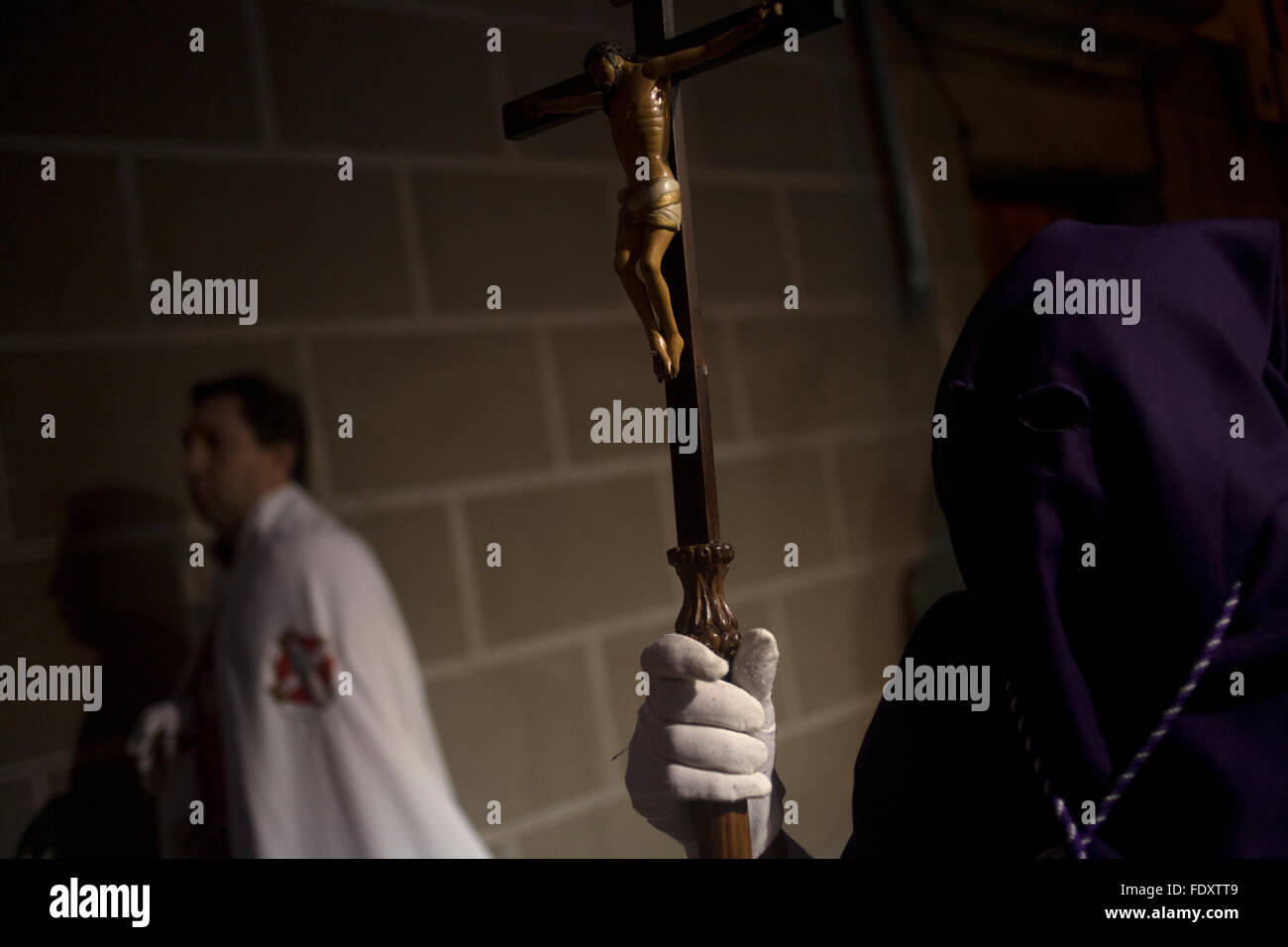 A Hooded Penitent Holds A Staff Decorated With Crucified Jesus During