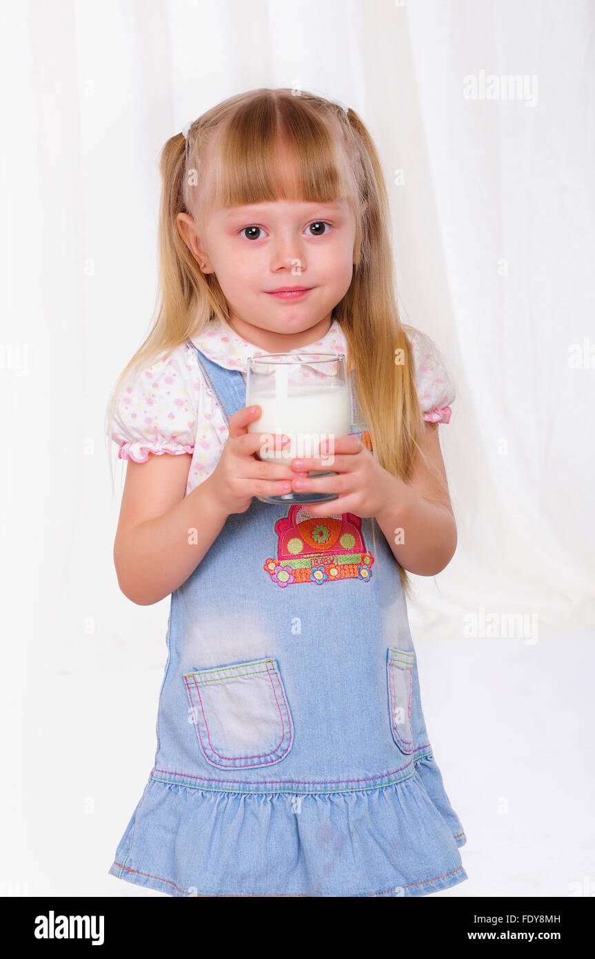 Little girl in blue dress drinks milk from a glass Stock Photo - Alamy
