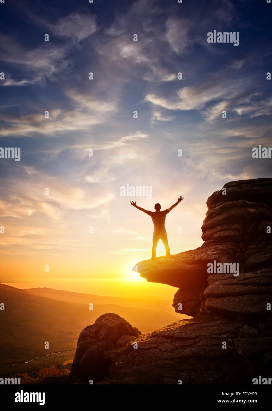 A person reaching up from a high point, set against a sunset. Expressing freedom Stock Photo