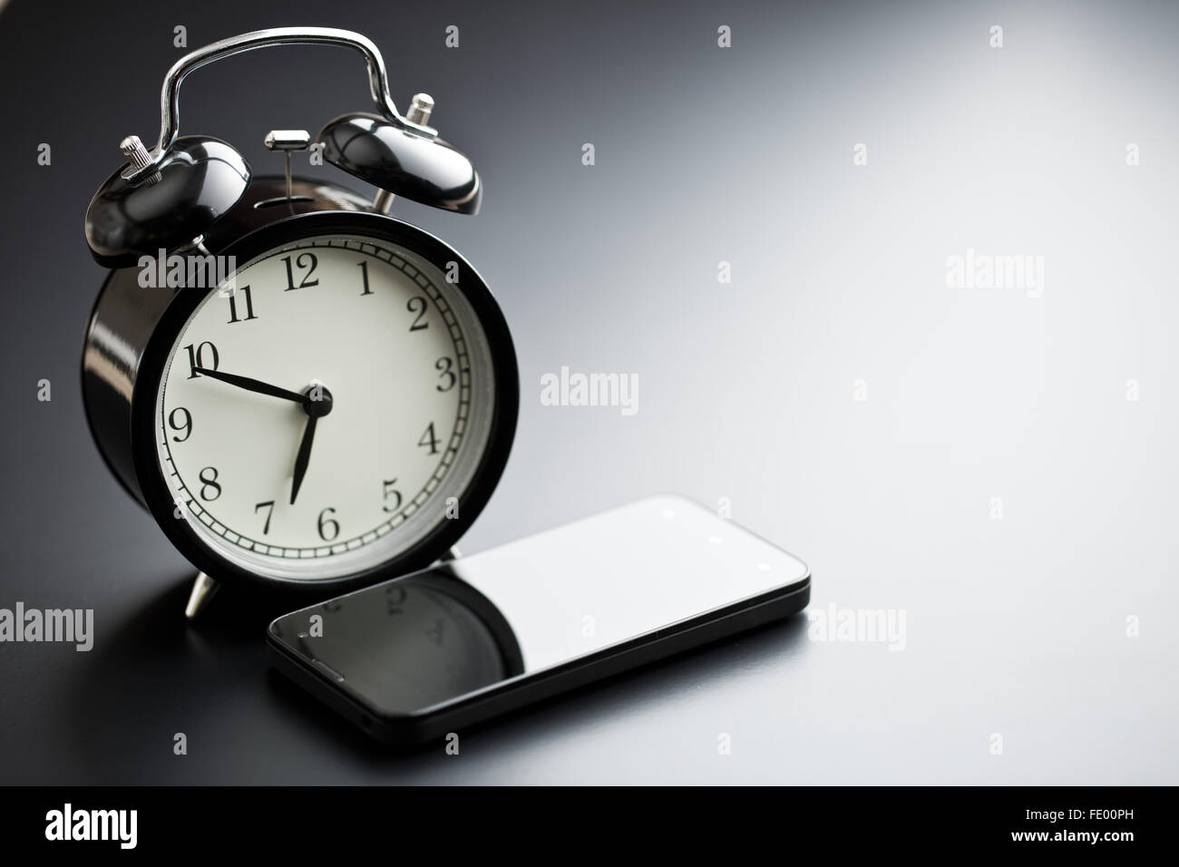 alarm clock with cellphone on black table Stock Photo