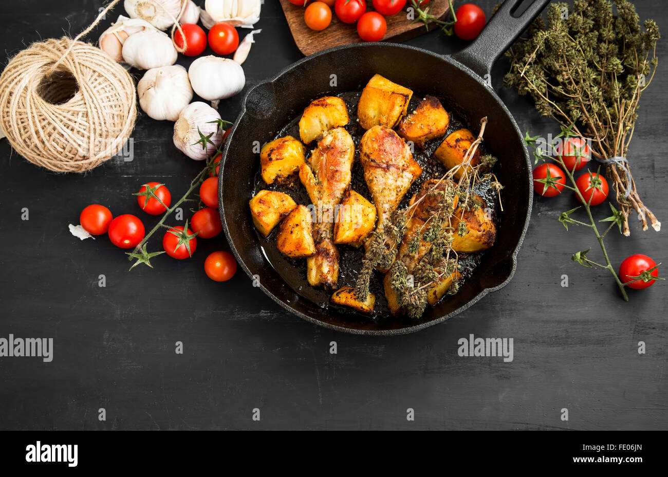 Roasted chicken legs with baked potatoes garnish and herbs in a cooking pan Stock Photo