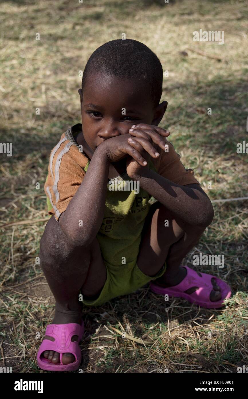 A young Ethiopian boy crouches down and watches the foreigners Stock Photo