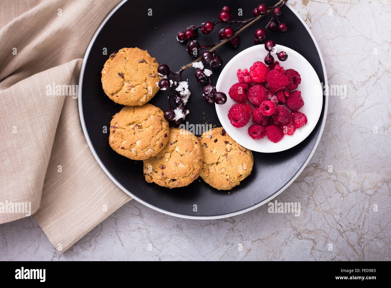 American Style White Chocolate Chip Cookie ob black plate served with Raspberries on marble Surface, cookies with Cranberries Stock Photo