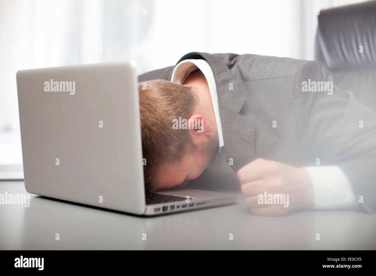 Desperate depressed businessman banging his fist on his desk and resting his head on the keyboard of his laptop computer Stock Photo