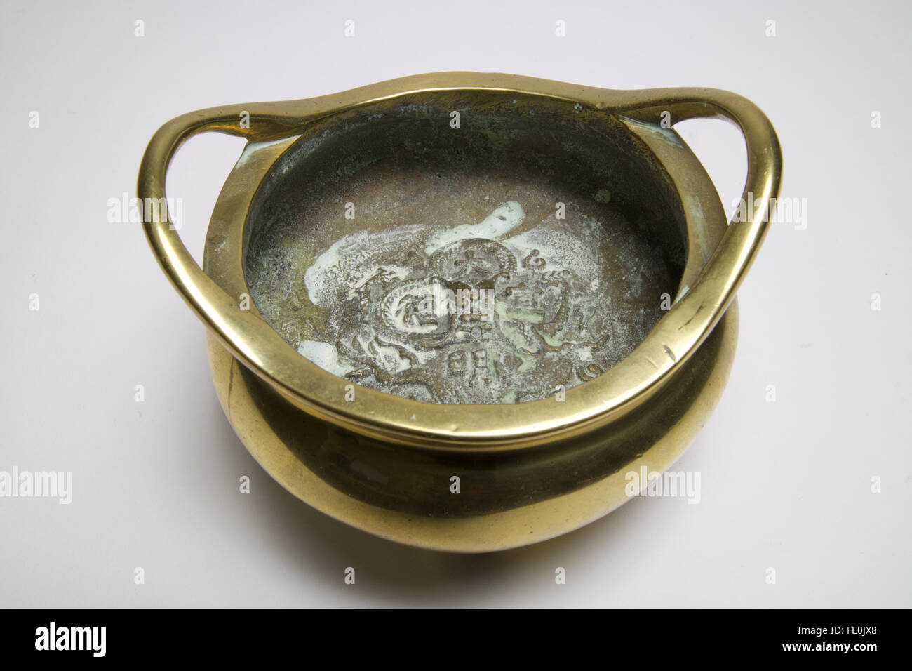 Antique Chinese bronze censer with twin handles and cast with a dragon to the inside and standing on three feet. Stock Photo