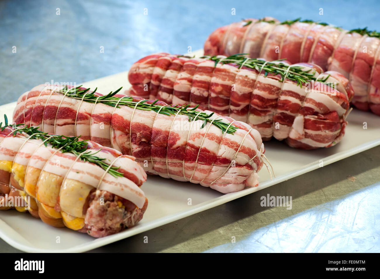 Single tray of prepared raw stuffed rolled veal meat wrapped with string and seasoned with rosemary sprigs Stock Photo