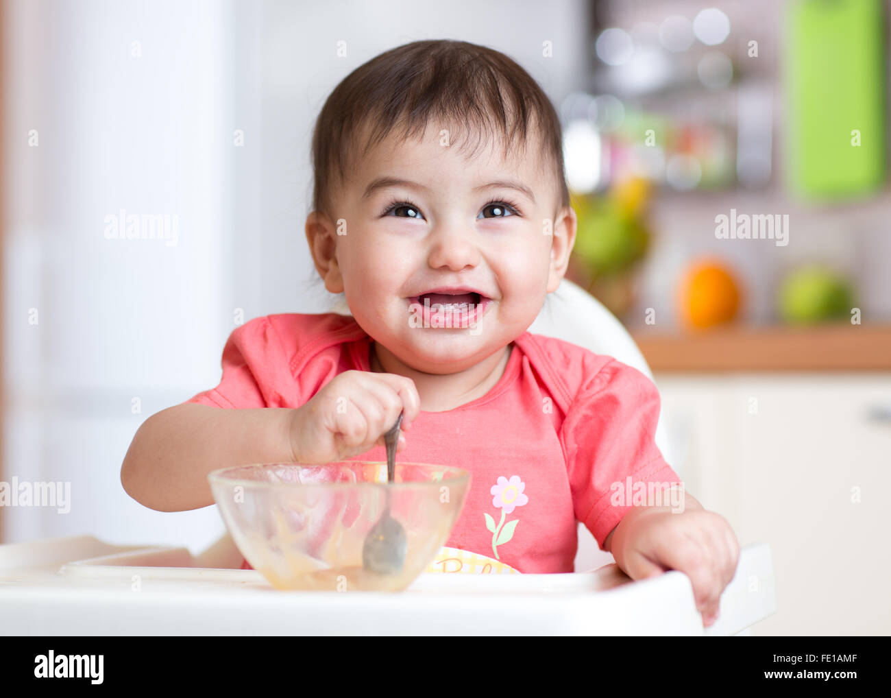 cheerful baby child eating food itself with a spoon Stock Photo