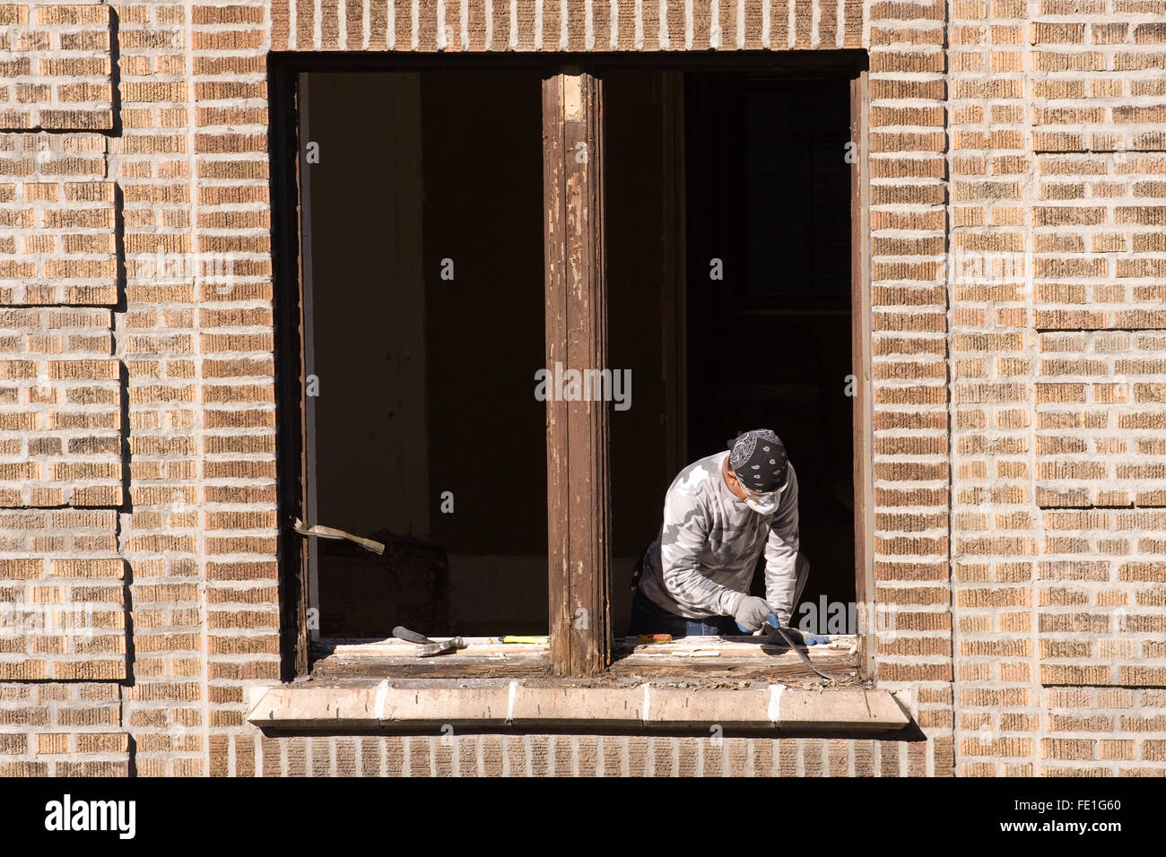 Construction Worker with a small pry bar removing and replacing a wooden window frame from a brick building Stock Photo