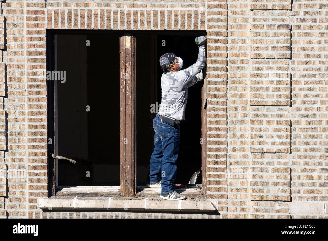 Construction Worker standing in an empty window opening in an apartment building and using a razor knife overhead Stock Photo