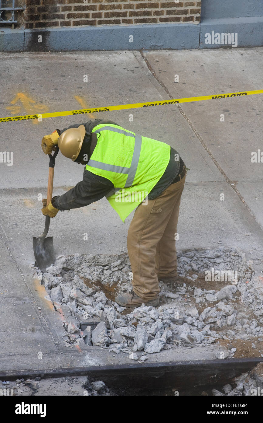 Construction Worker manually removing broken concrete debris from a hole in the sidewalk with a shovel (FE1G87, FE1G8A, FE1G8C) Stock Photo