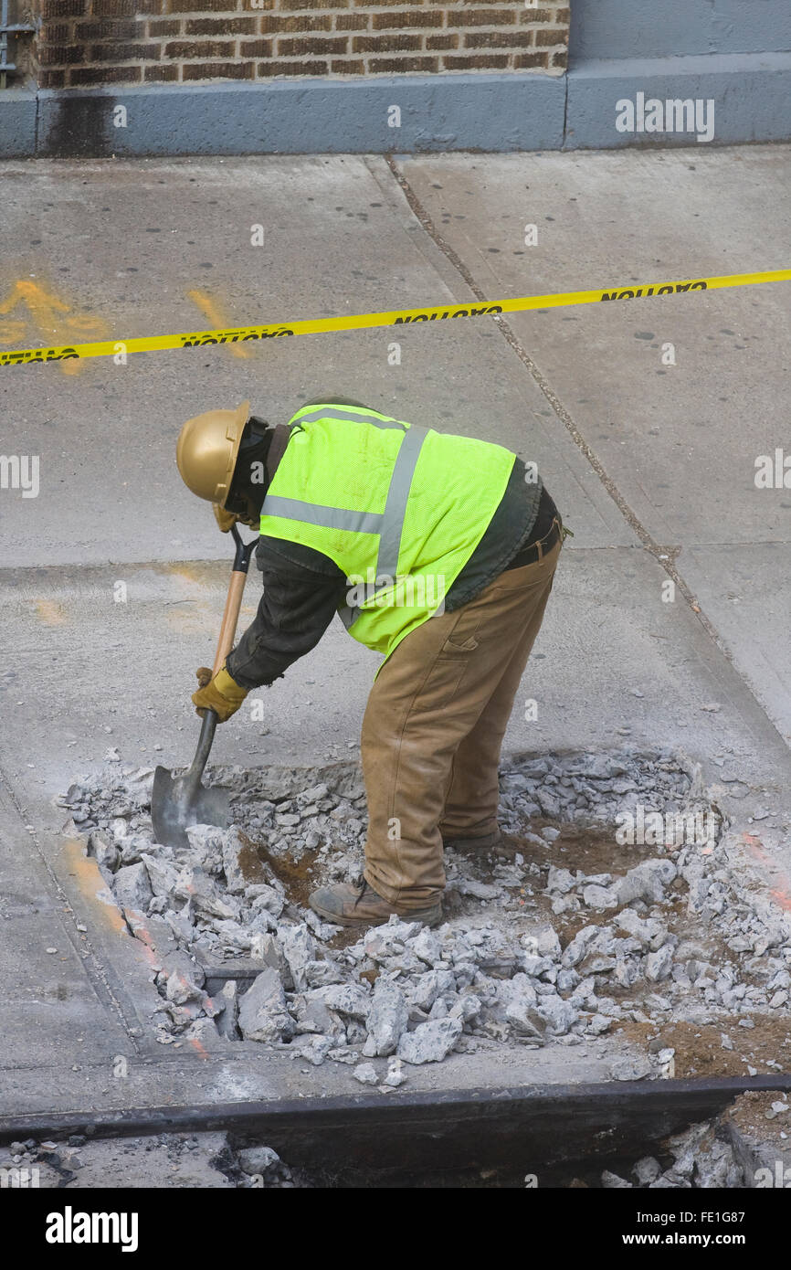Construction Worker manually removing broken concrete debris from a hole in the sidewalk with a shovel (FE1G84, FE1G8A, FE1G8C) Stock Photo