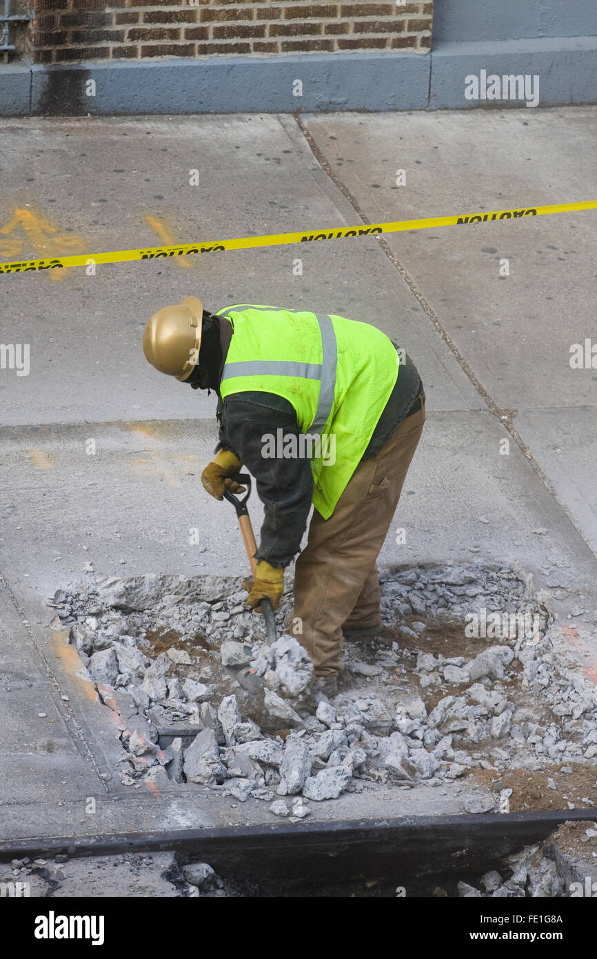 Construction Worker manually removing broken concrete debris from a hole in the sidewalk with a shovel (FE1G84, FE1G87, FE1G8C) Stock Photo