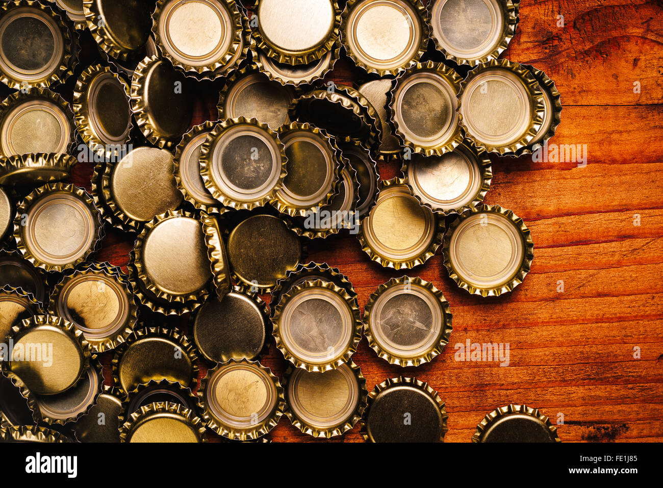 Large pile of beer bottle caps on rustic oak wooden desk Stock Photo