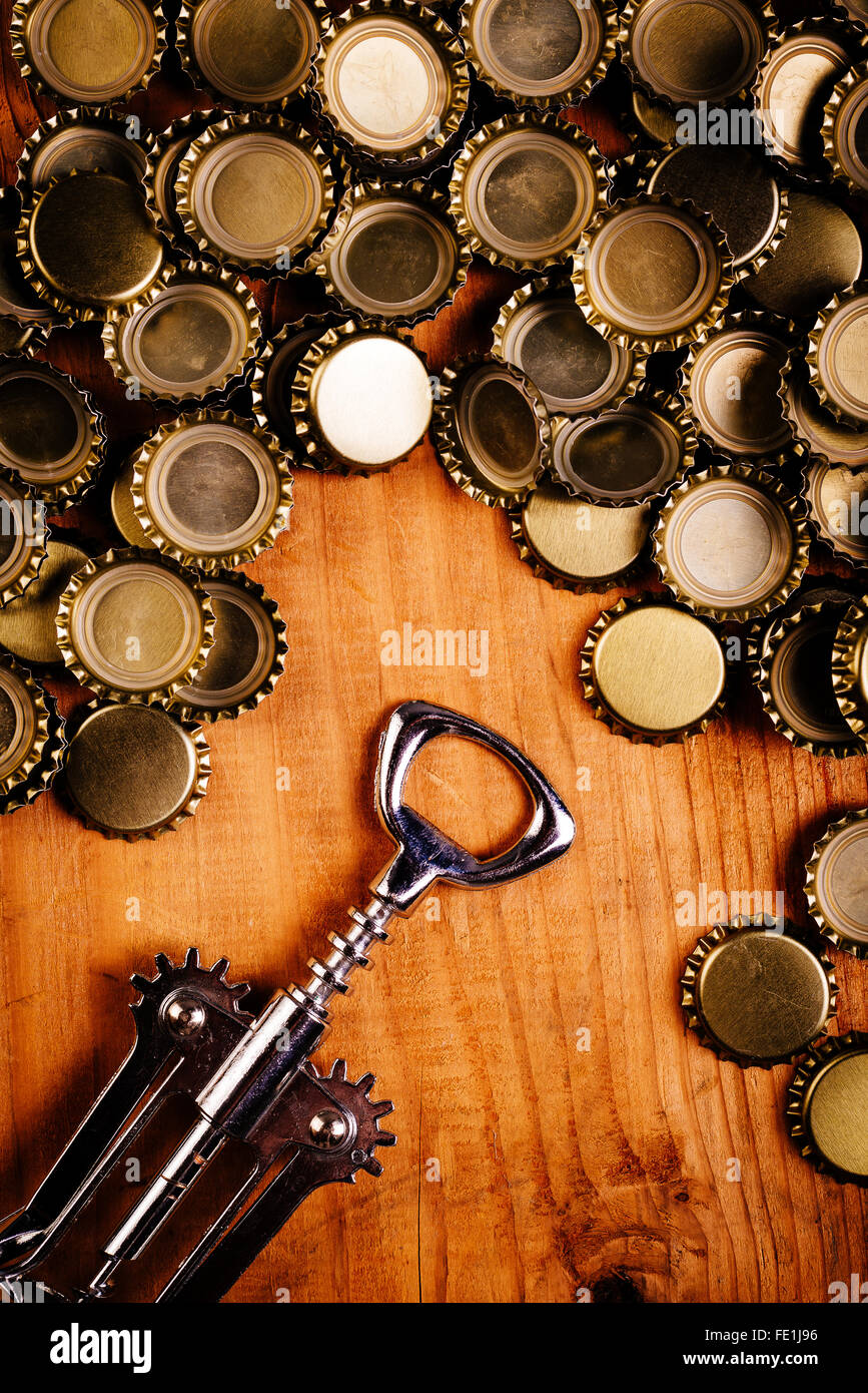 Classic bottle opener and pile of beer bottle caps on top of rustic oak wood desk, top view. Stock Photo