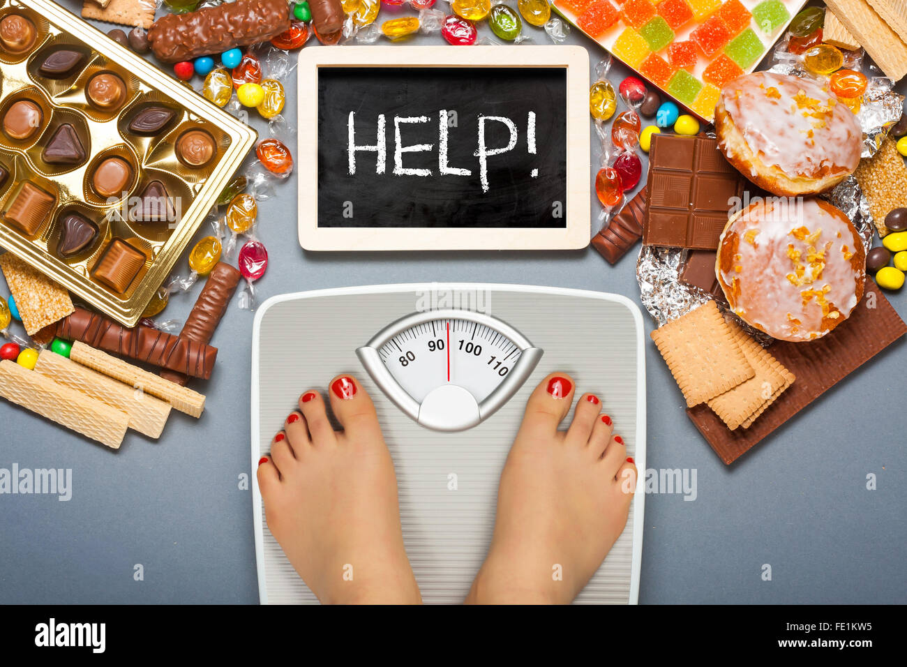 Unhealthy diet - overweight. Feet on bathroom scale and chocolate, jelly cubes, candies, chocolate bars, cookies, donuts Stock Photo