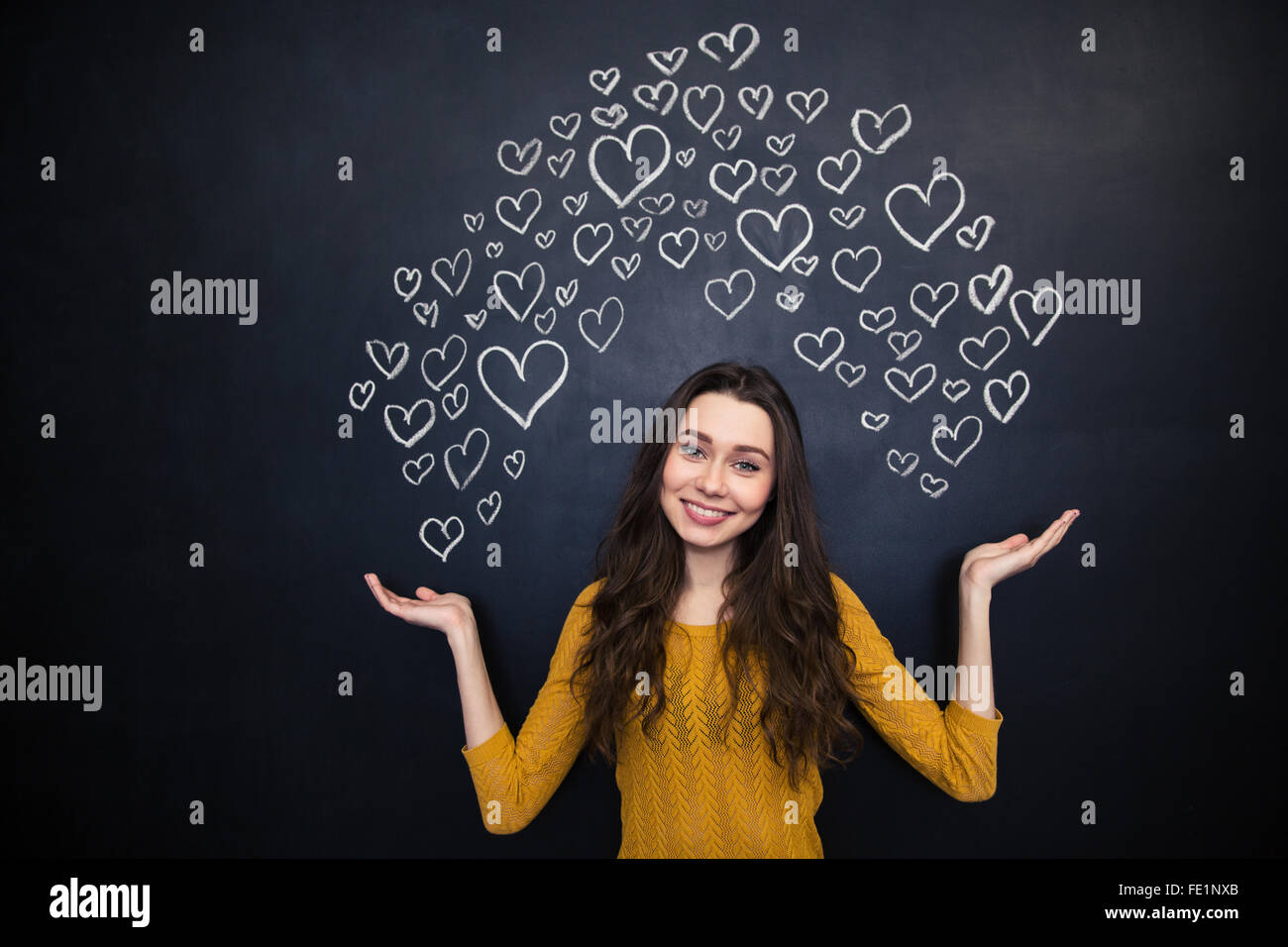 Beautiful smiling young woman holding drawing hearts on both palms over blackboard background Stock Photo