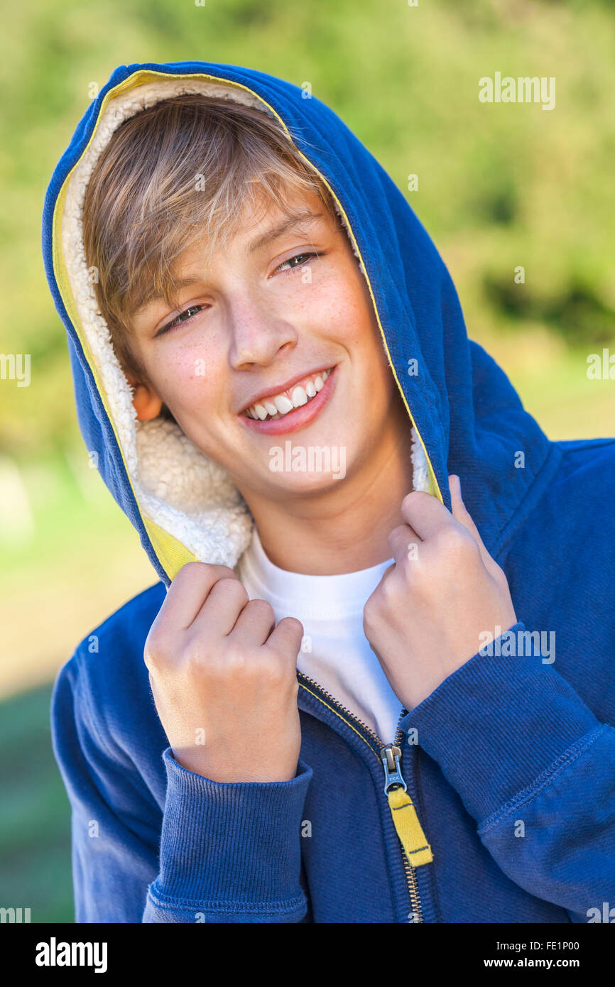 Young happy laughing male boy teenager blond child outside in summer sunshine wearing a blue hoody Stock Photo