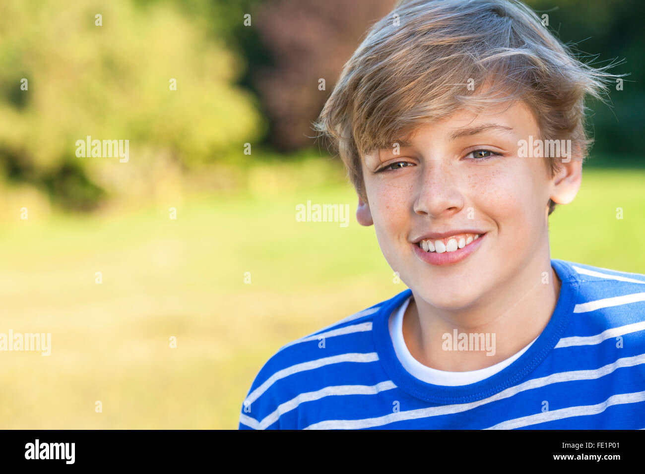 Young happy smiling male boy teenager blond child outside in summer sunshine wearing a blue sweatshirt Stock Photo