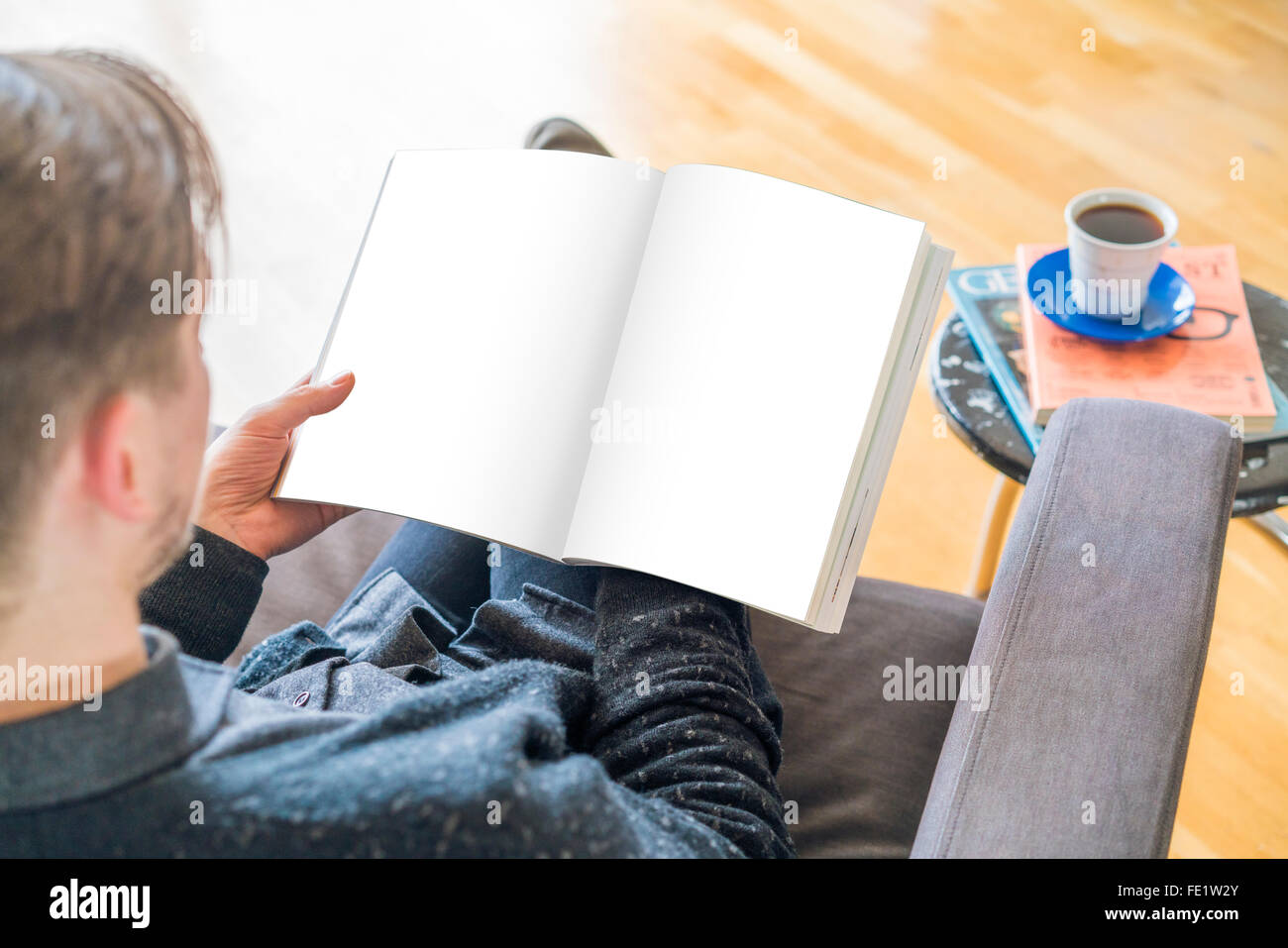 YOUNG EUROPEAN FASHIONABLE MALE READS A MAGAZINE BOOK IN A COFFEE SHOP. BLANK PAGES Stock Photo