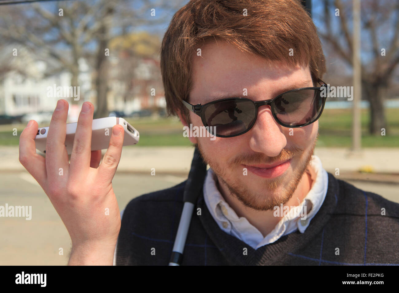Young blind man in his neighborhood using assistive technology with his cell phone Stock Photo