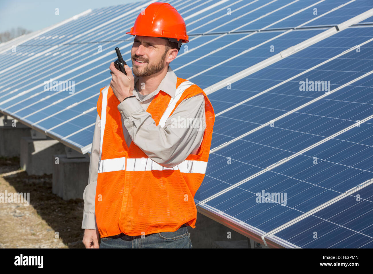 Power engineer standing at solar photovoltaic array and on radio Stock Photo