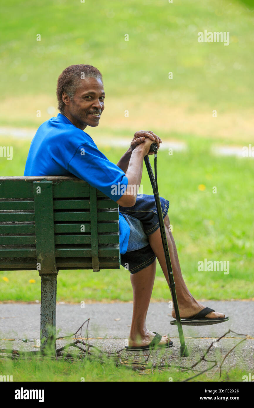 Man with Traumatic Brain Injury relaxing with his cane in a park Stock Photo