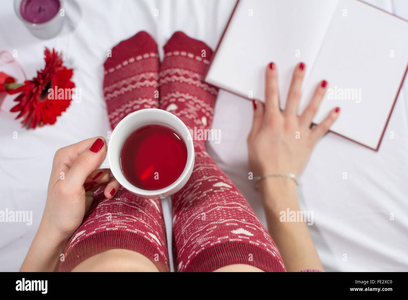 Woman having a cup of tea in bed and reading a book Stock Photo