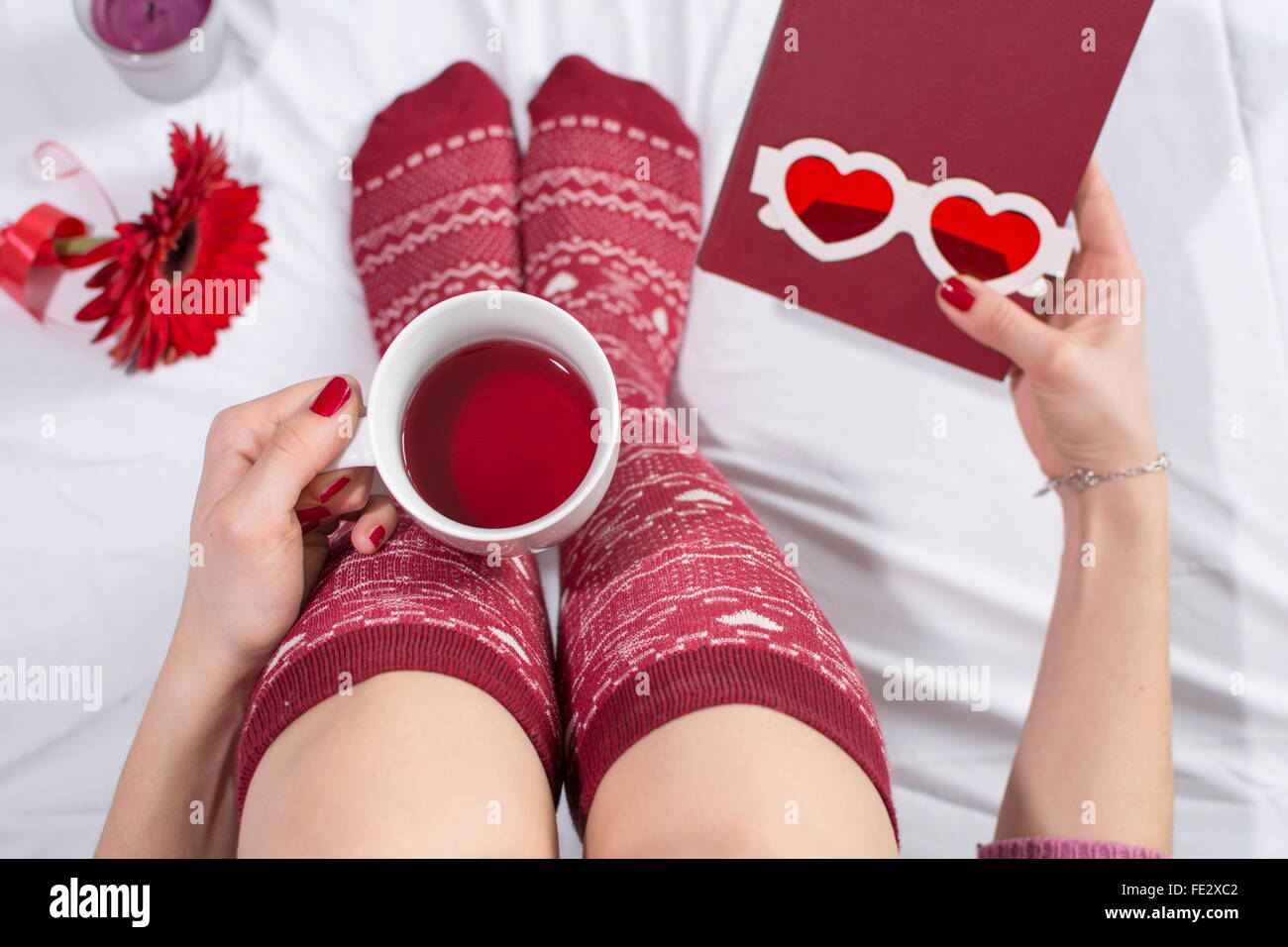 Woman having a cup of tea in bed and holding a love novel Stock Photo