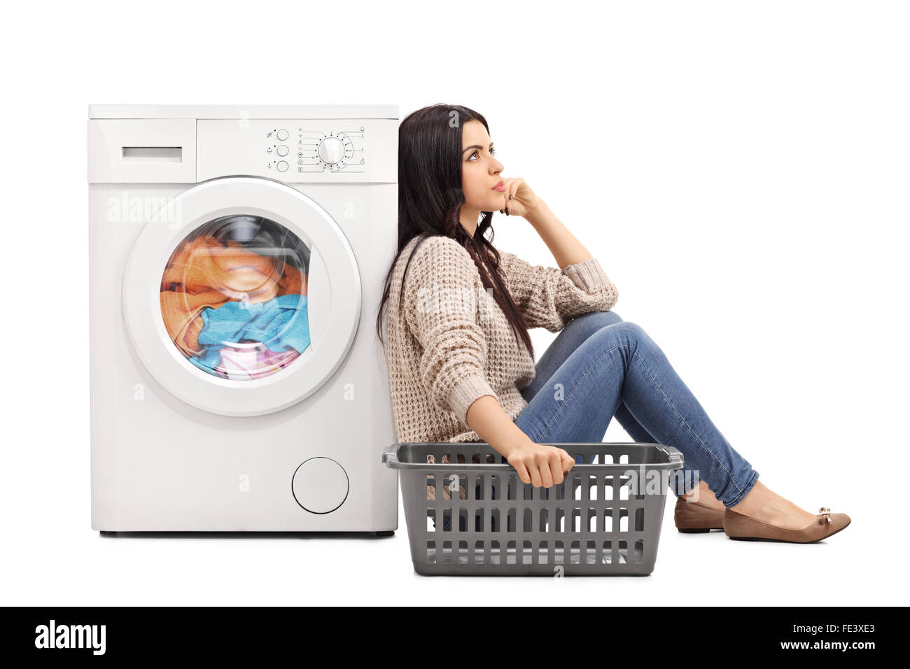 Young bored woman sitting by a washing machine and waiting for the laundry isolated on white background Stock Photo