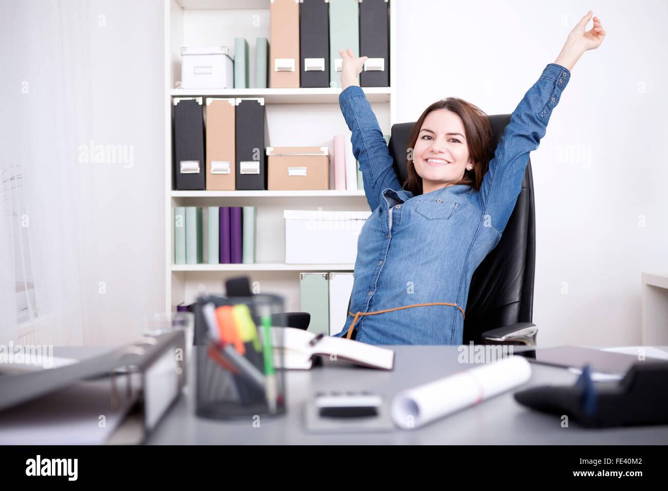 Happy Young Office Woman Sitting on her Chair Stretching her Arms While Looking at the Camera. Stock Photo