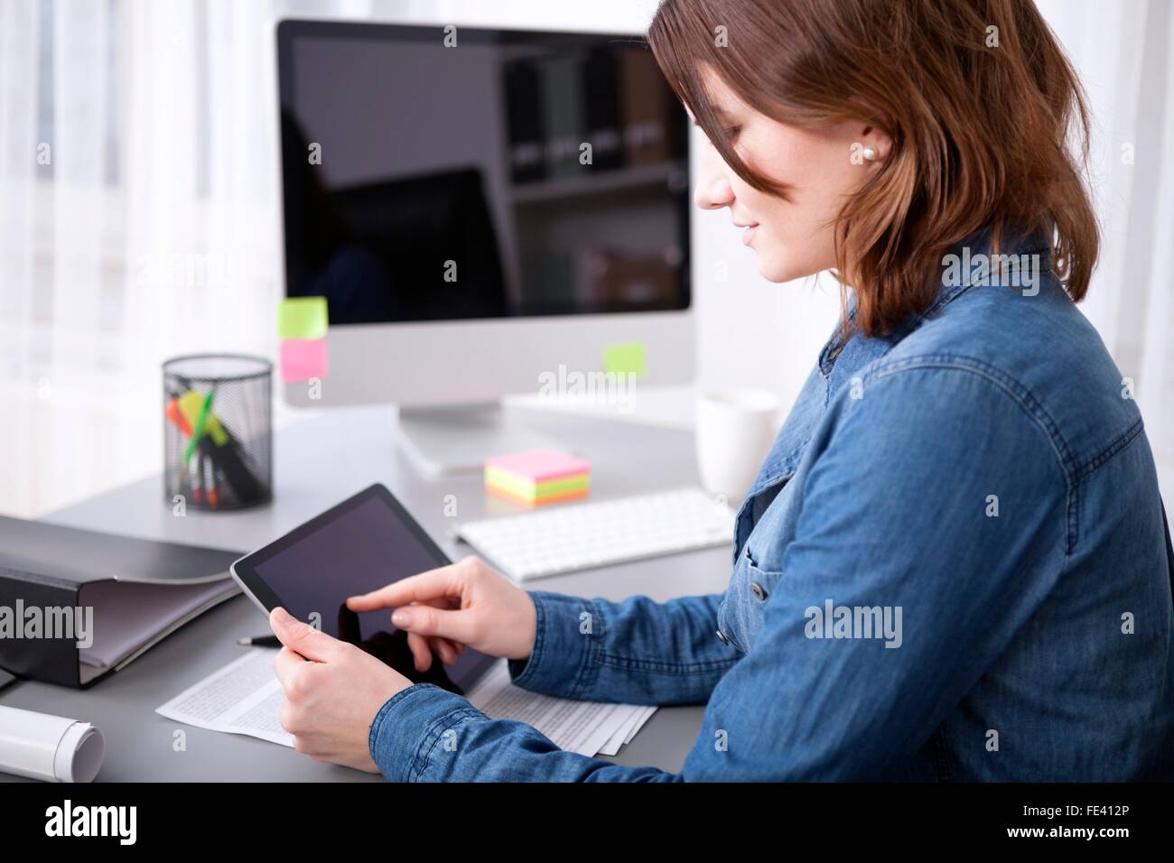 Side view of an attractive young businesswoman surfing the internet on her tablet computer as she sits at the desk Stock Photo