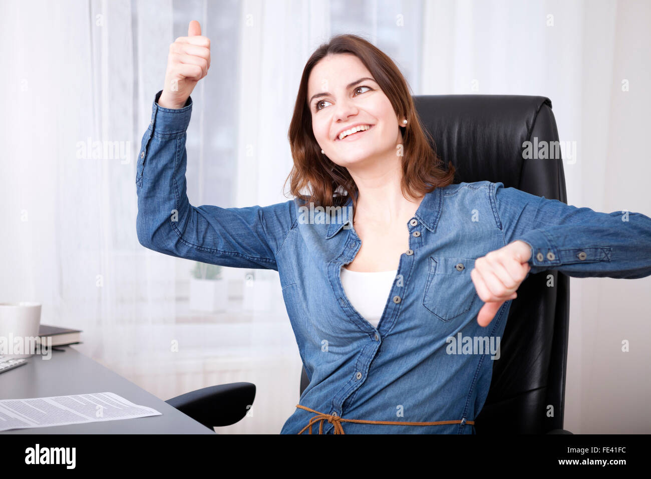 Undecided businesswoman laughing playfully and giving a thumbs up and down gesture simultaneously Stock Photo