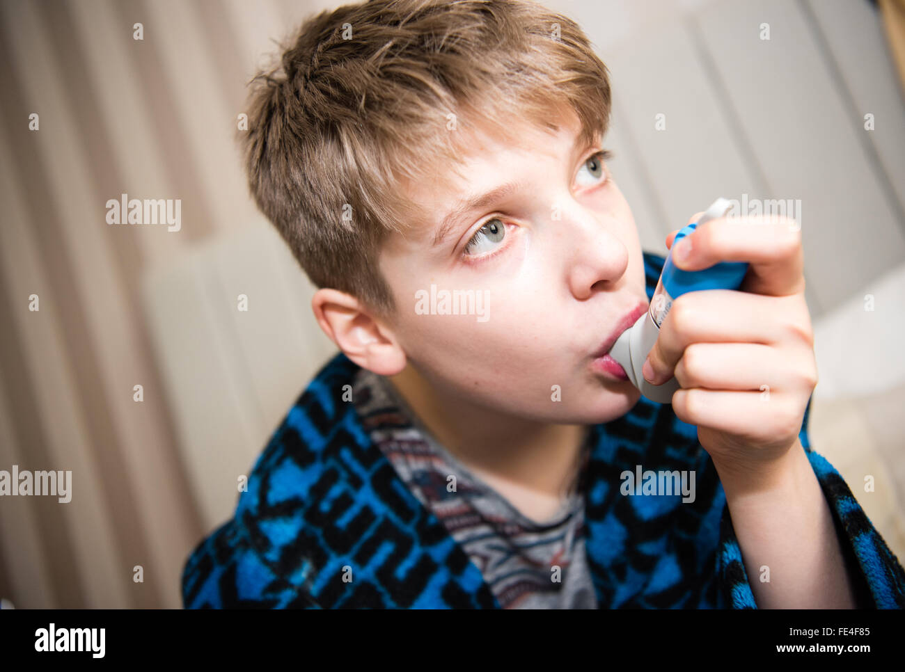 Poorly white teenage boy suffering a dangerous asthma attack taking breaths through a spacer and his inhaler to get ventolin to help him breath Stock Photo