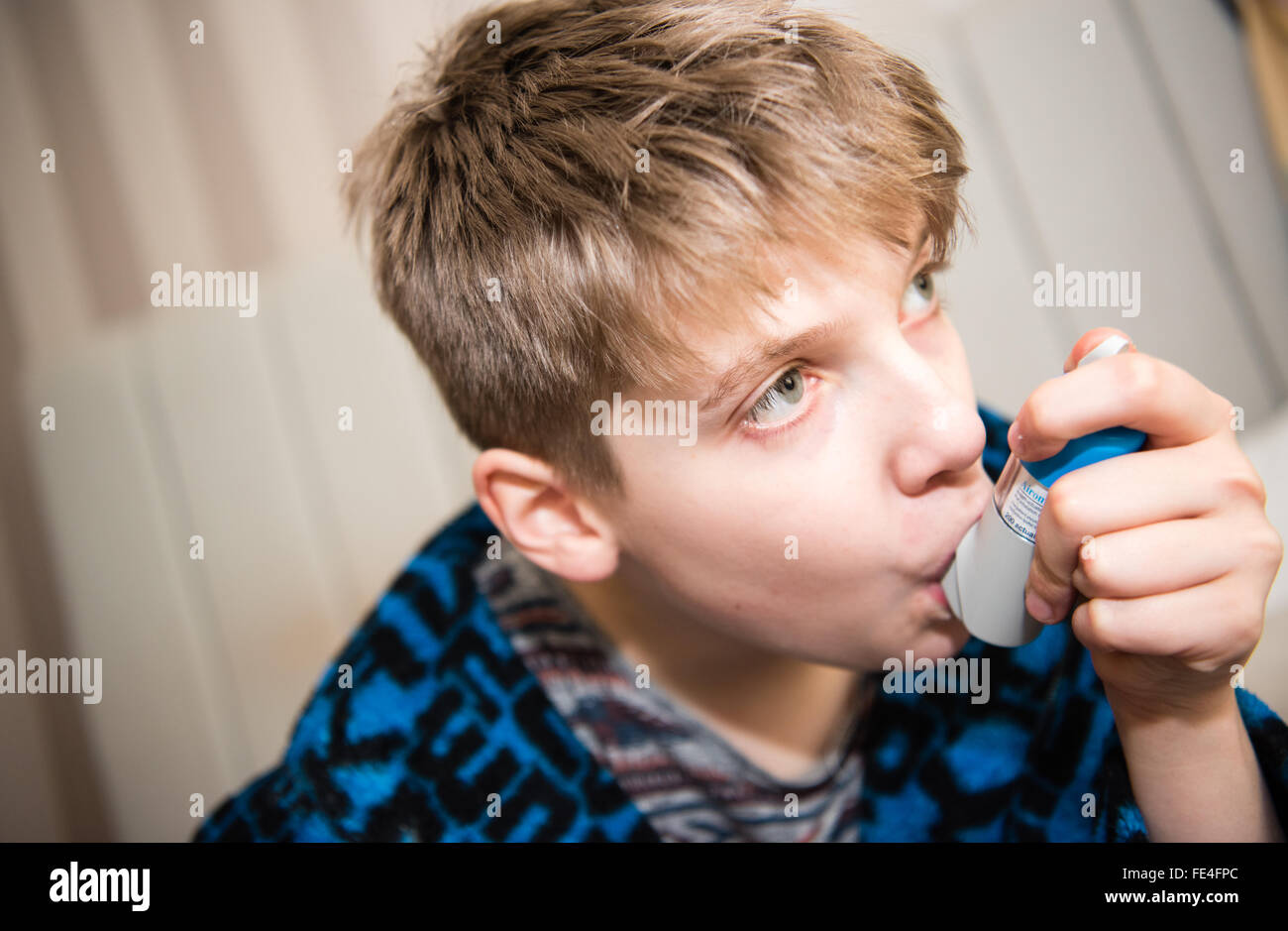 Poorly white teenage boy suffering a dangerous asthma attack taking breaths through a spacer and his inhaler to get ventolin to help him breath Stock Photo