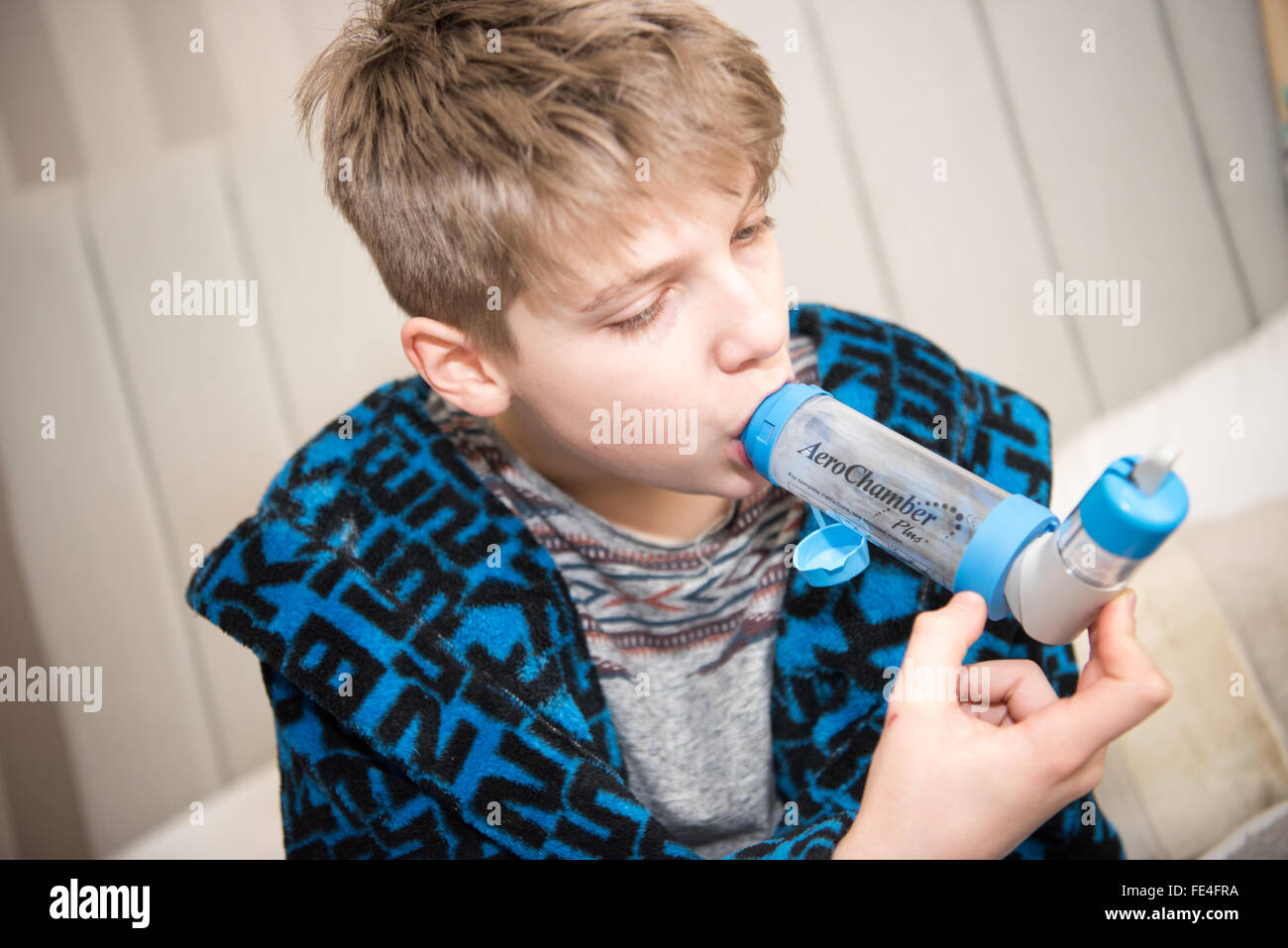 Poorly white teenage boy suffering a dangerous asthma attack taking breaths through a spacer and his inhaler to get ventolin to help him breath Stock Photo